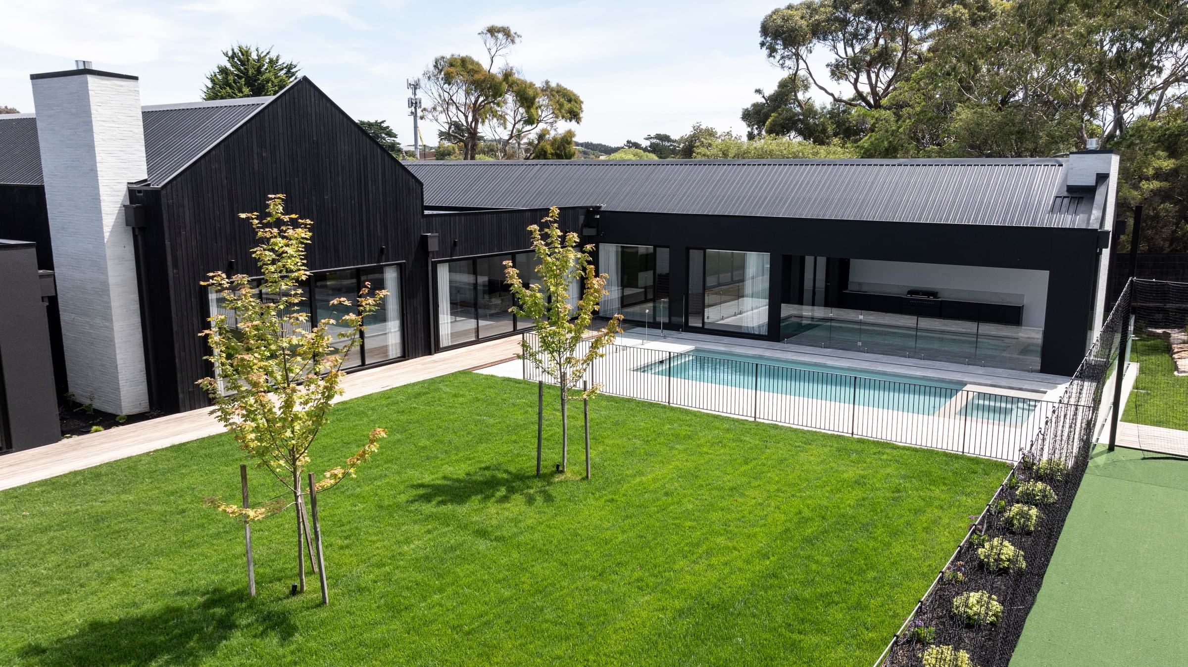 Sanctuary fibreglass pool set into a broad lawn beside a black home