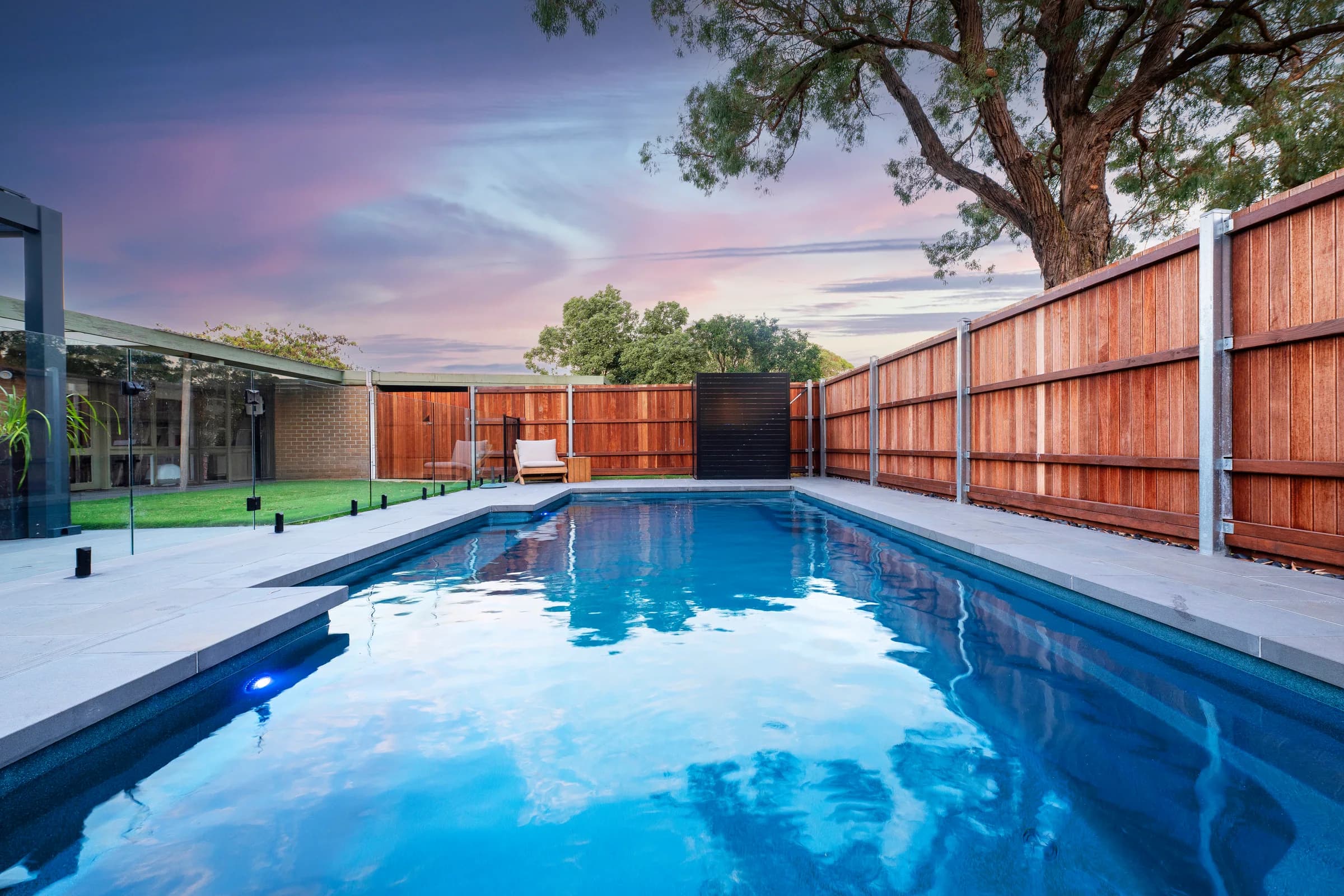Sapphire fibreglass pool at dusk beside a timber boundary fence in Berwick