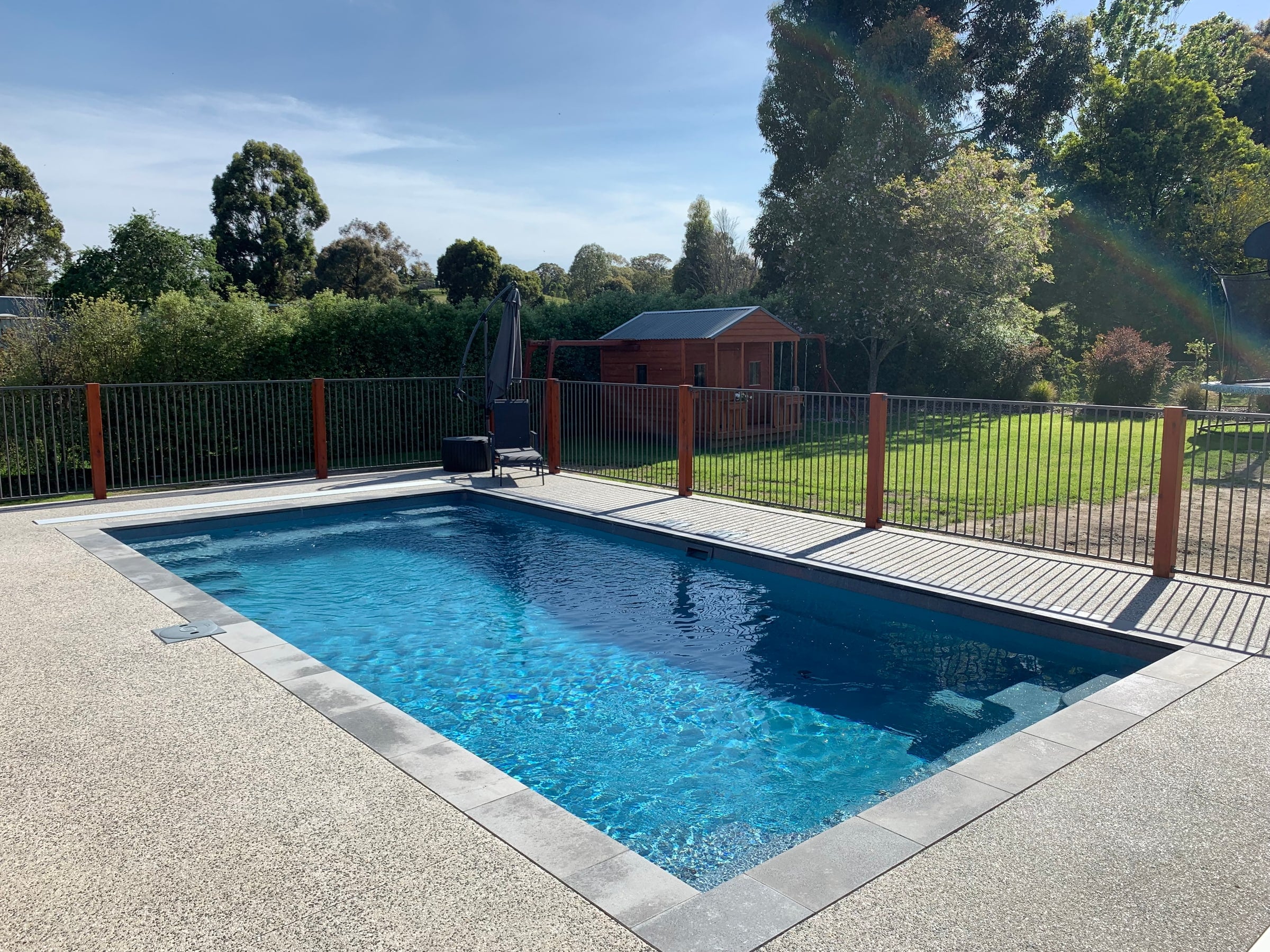 Contemporary fibreglass pool with paved surrounds and a fenced lawn