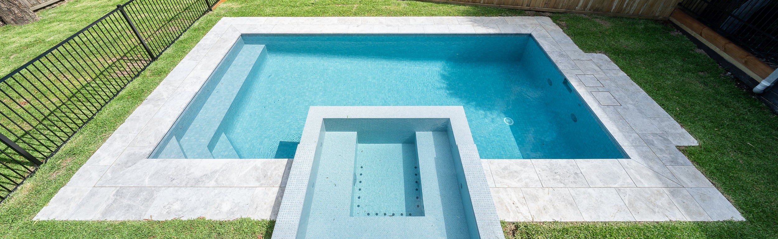 A completed Enchanted Pools concrete pool and raised spa within a residential backyard