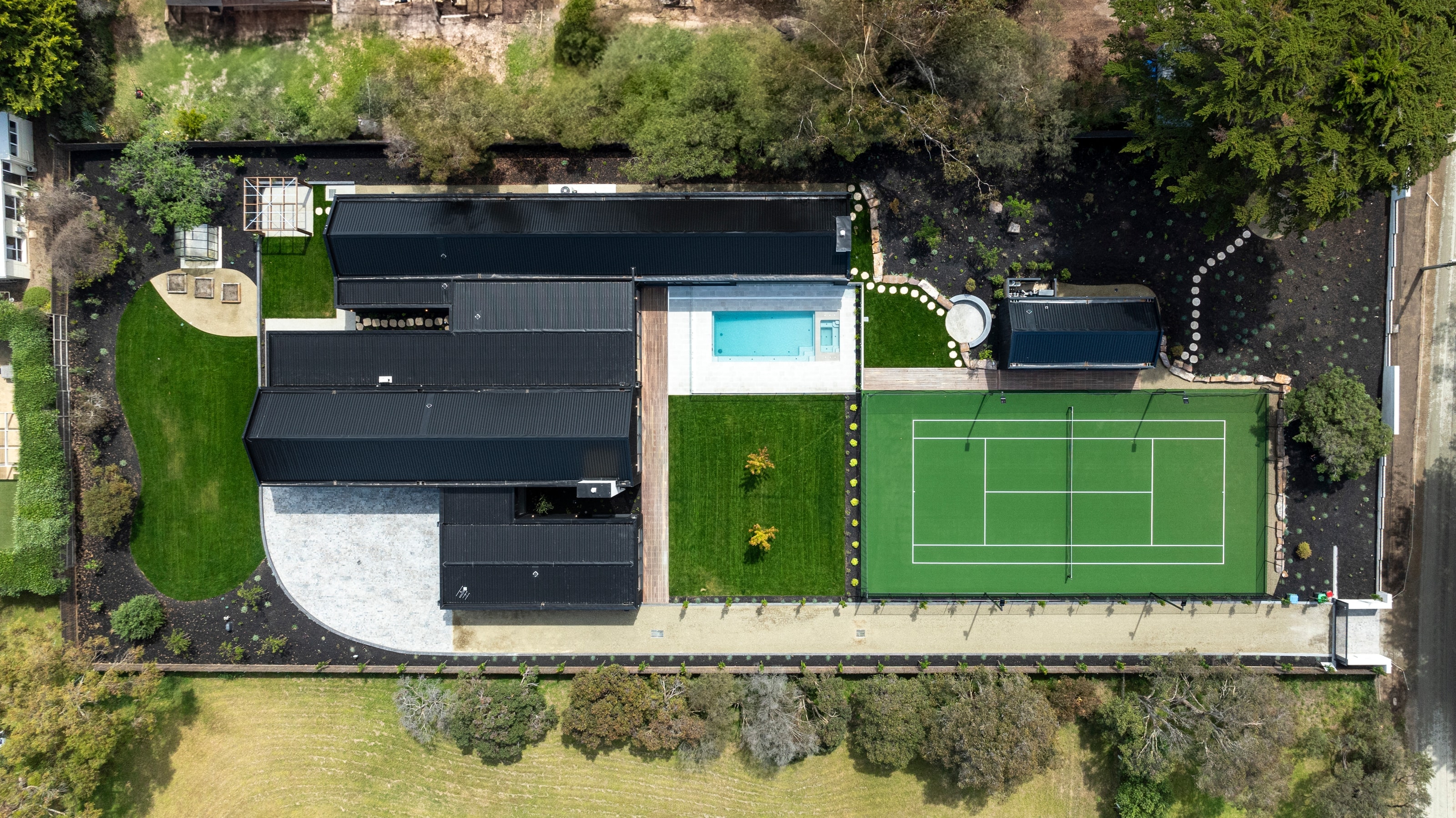 Aerial view of a Sanctuary pool, black home and tennis court
