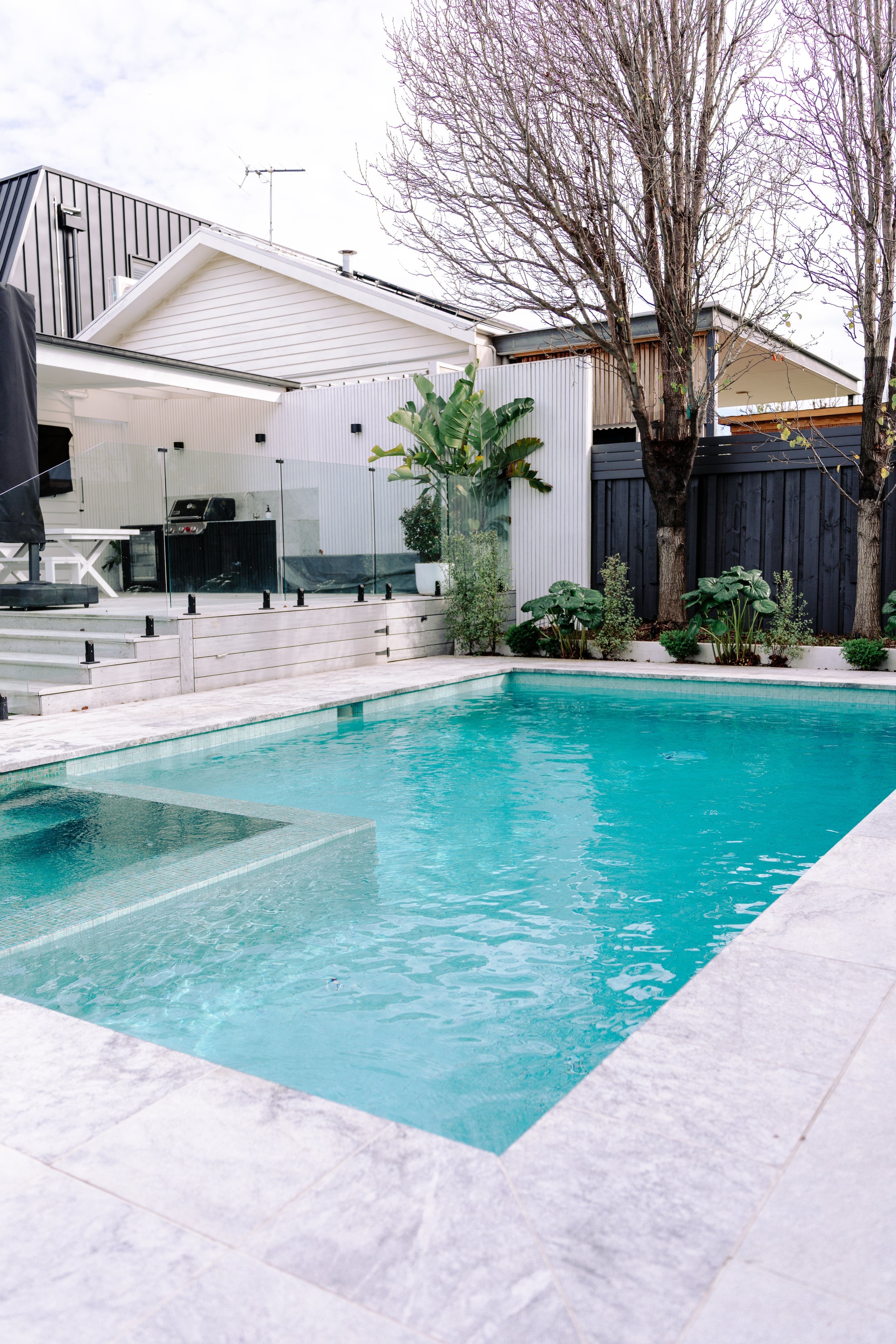 Pale stone pool surrounds beside the white weatherboard home in Bentleigh
