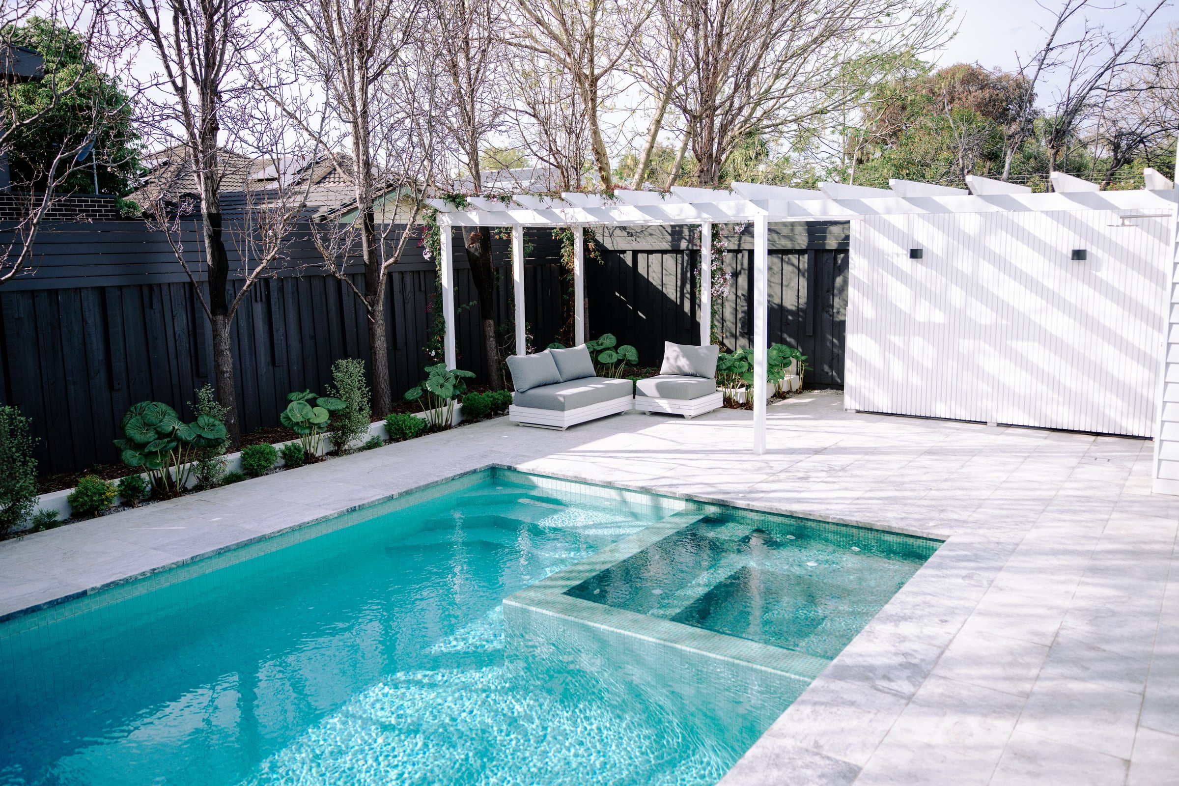 Pool and spa framed by a white pergola and established trees