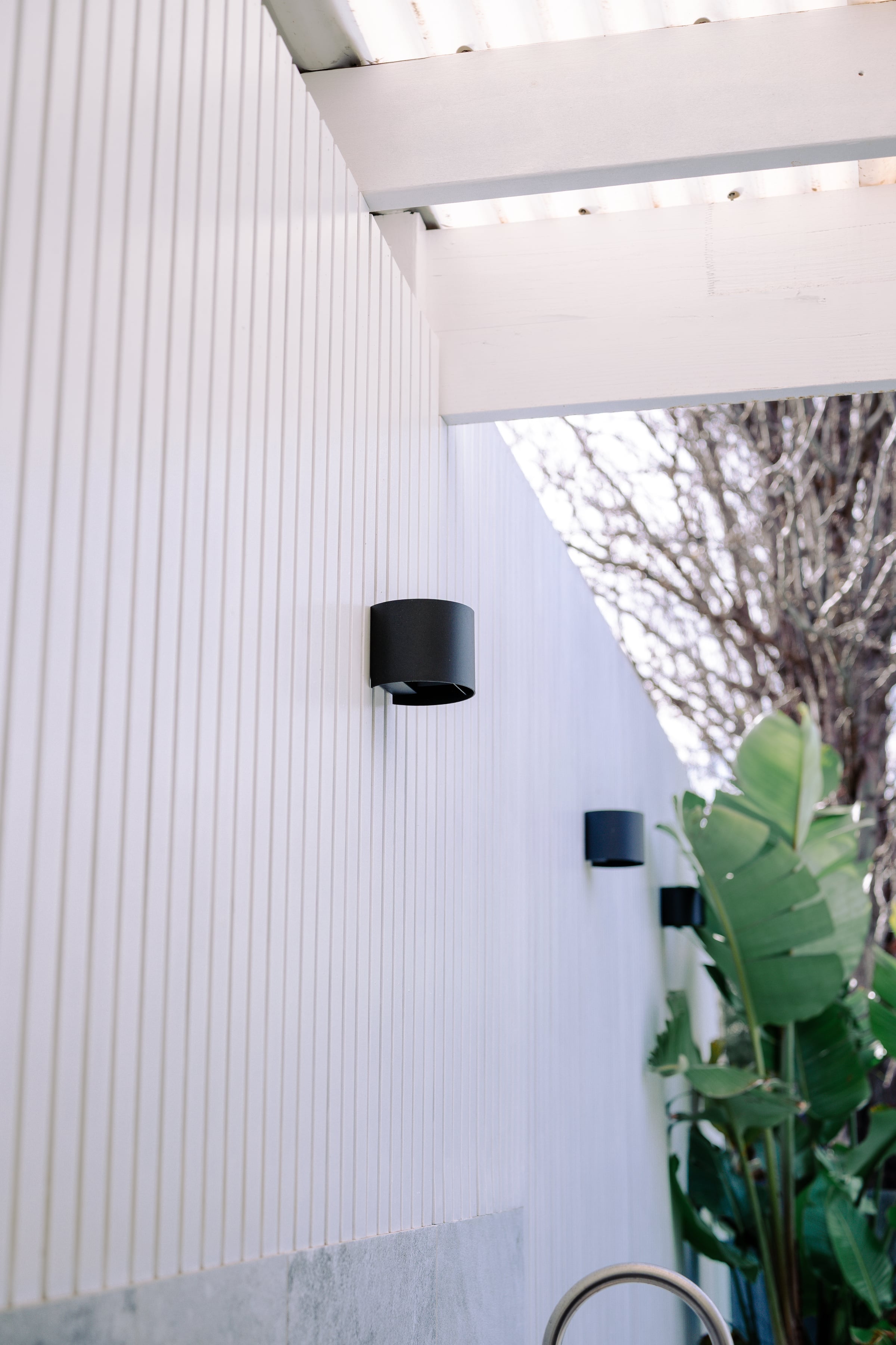 Outdoor shower against the white weatherboard wall beside the pool