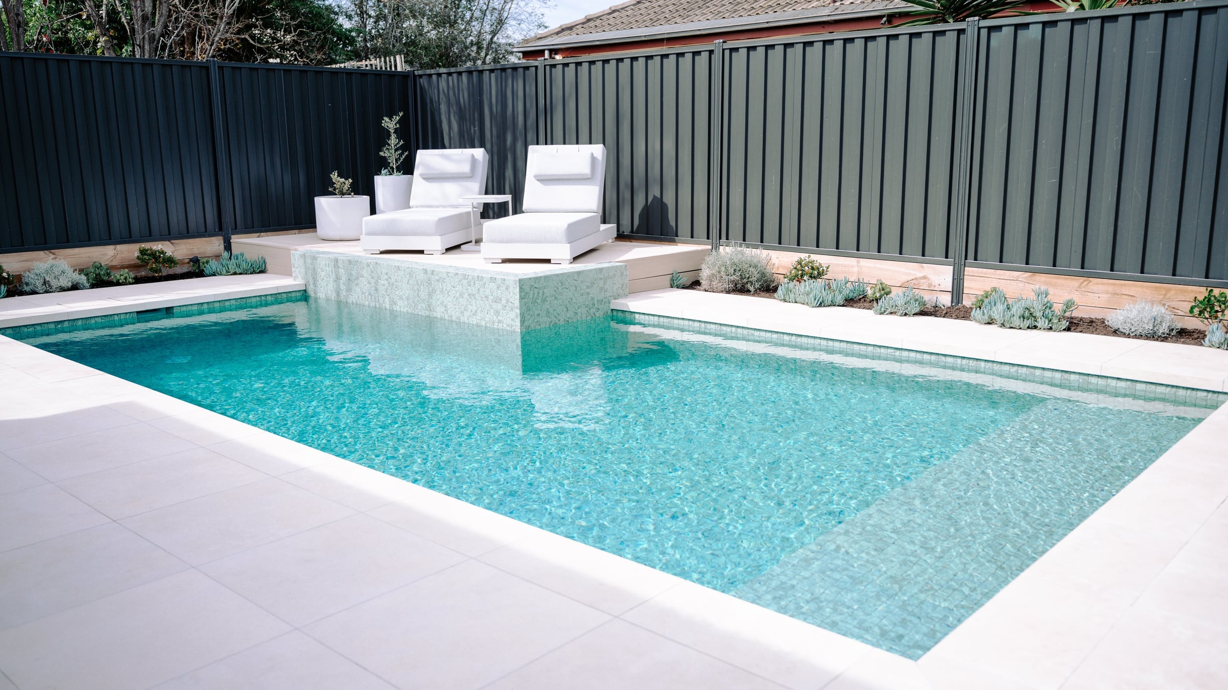 Bentleigh East concrete pool with a raised tiled wall and two white sun lounges on the deck