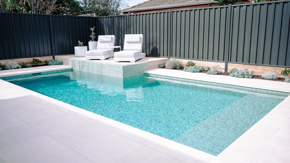 Bentleigh East concrete pool with a raised tiled wall and two white sun lounges on the deck