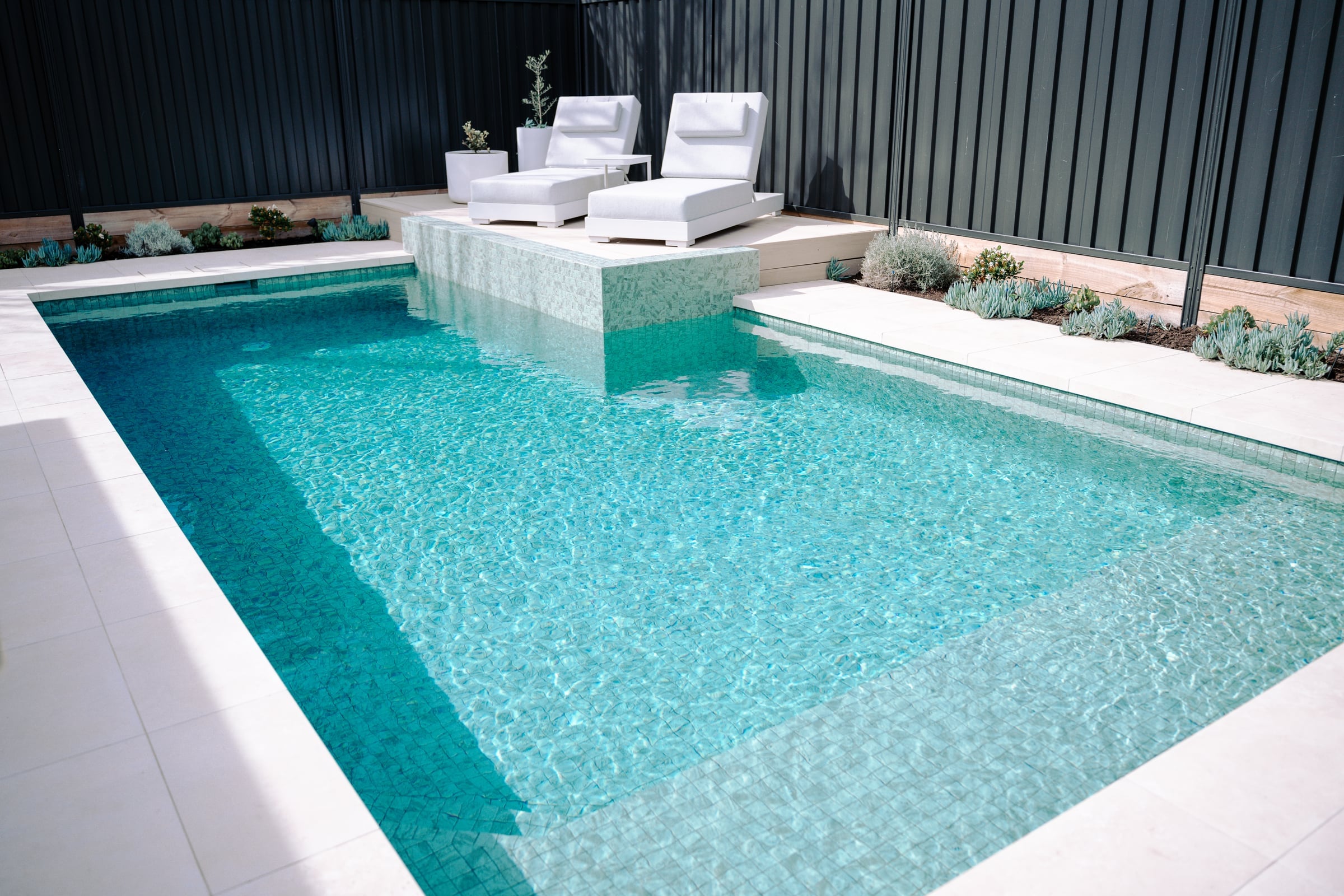 Wide view of the pool, pale surrounds and timber sunbaking platform